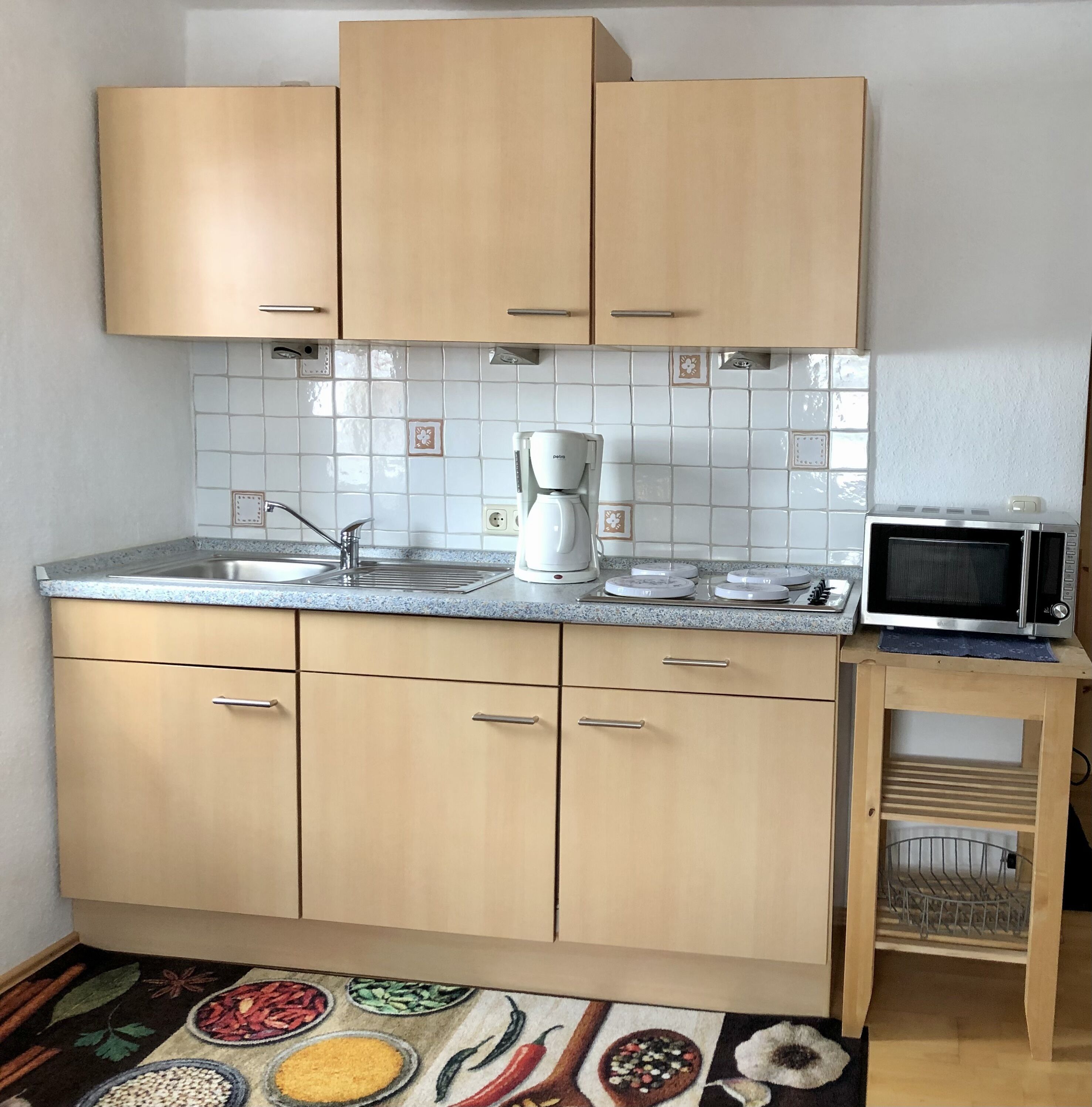 Een kleine keuken met houten kastjes, een ingebouwde magnetron en een koffiezetapparaat.