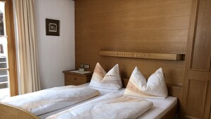 A double bed with a wooden headboard, a nightstand with a clock, and a framed picture on the wall. - (2) Zwei-Raum-Ferienwohnung 40qm, 1-4 Personen, Extra-Schalfzimmer, Wohnküche, große Balkonterrasse (Reit im Winkl)