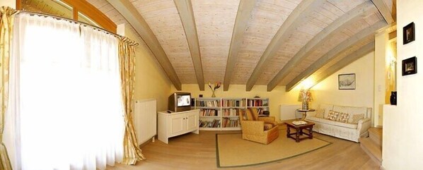 A cozy living room with a wooden ceiling, a bookshelf, a television, and a sofa.