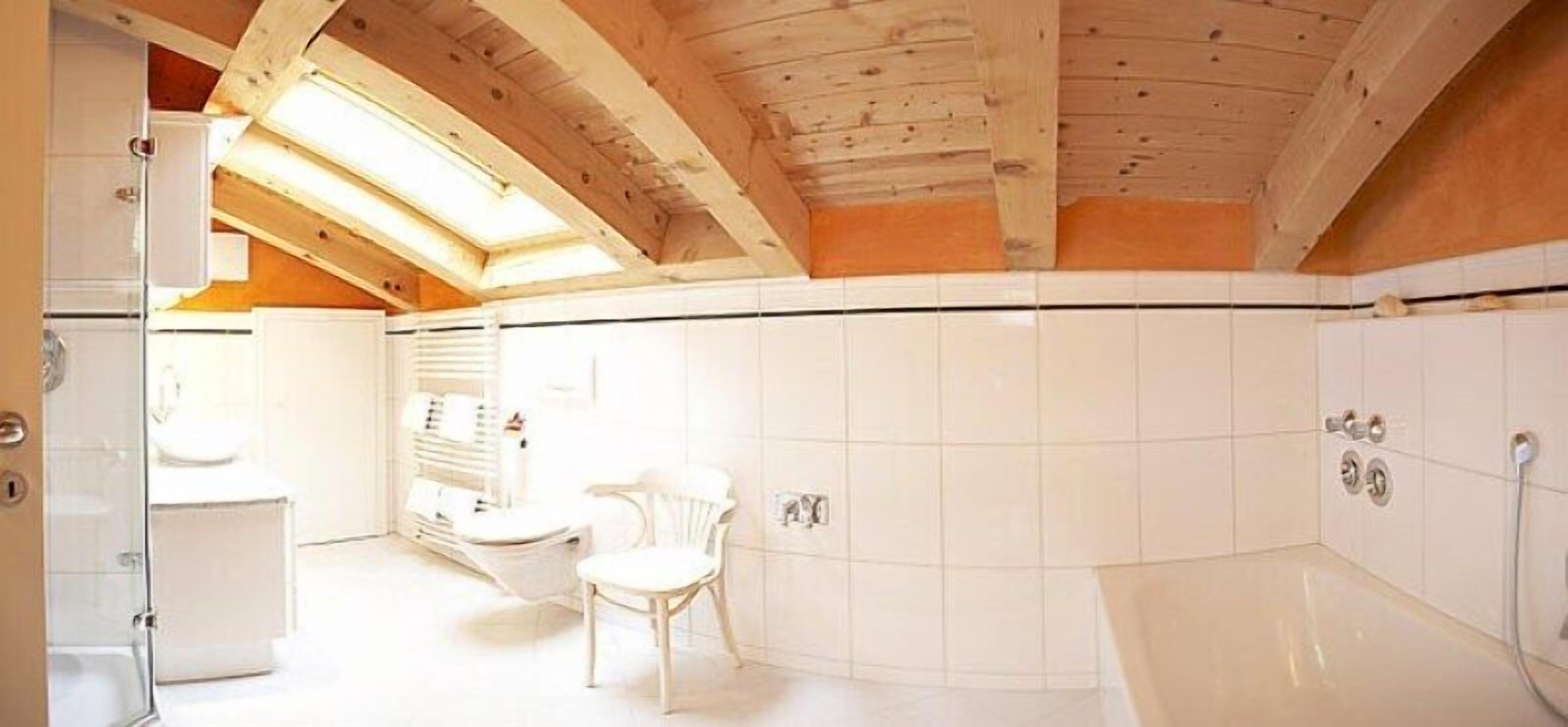 A bathroom with a skylight, white tiles, a bathtub, and a toilet.