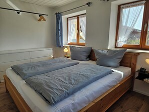 A double bed with a wooden headboard, a bedside table with a lamp, and a window with curtains.
