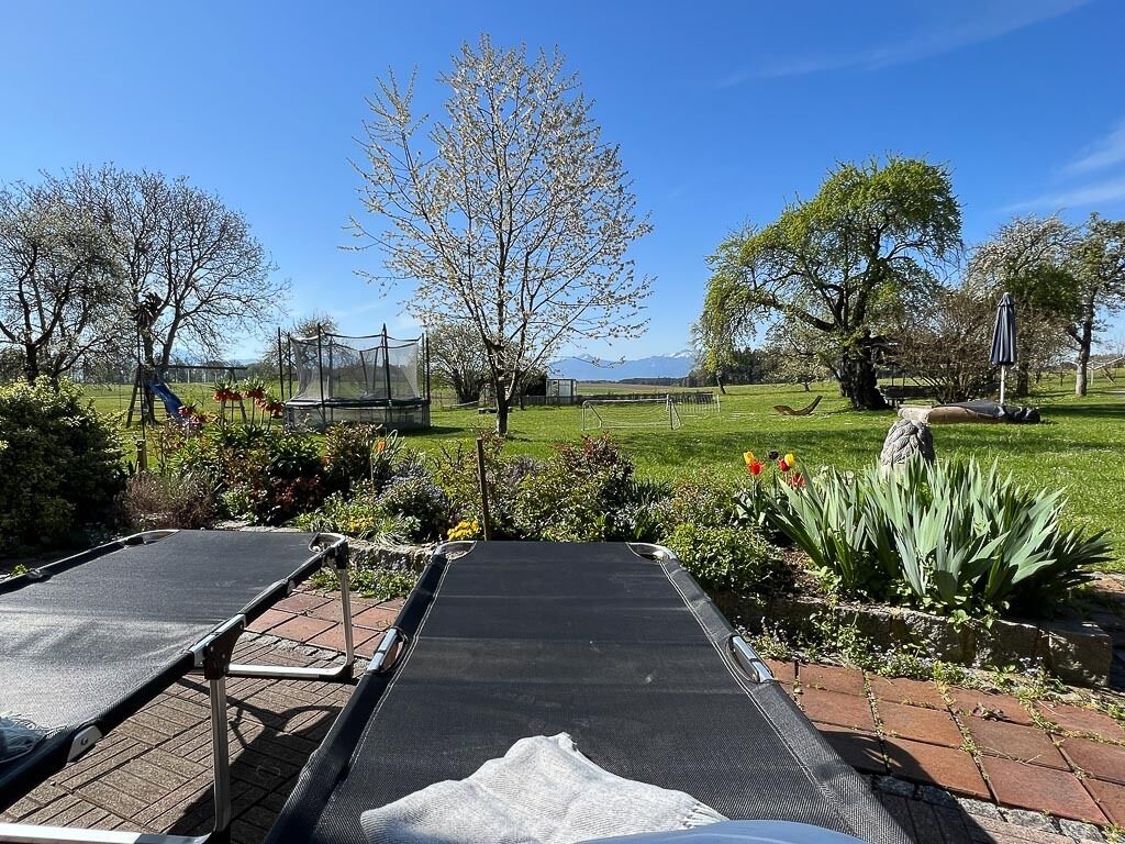 Ein Garten mit Trampolin, Spielgerüst und Blick auf ein Feld und Berge in der Ferne.