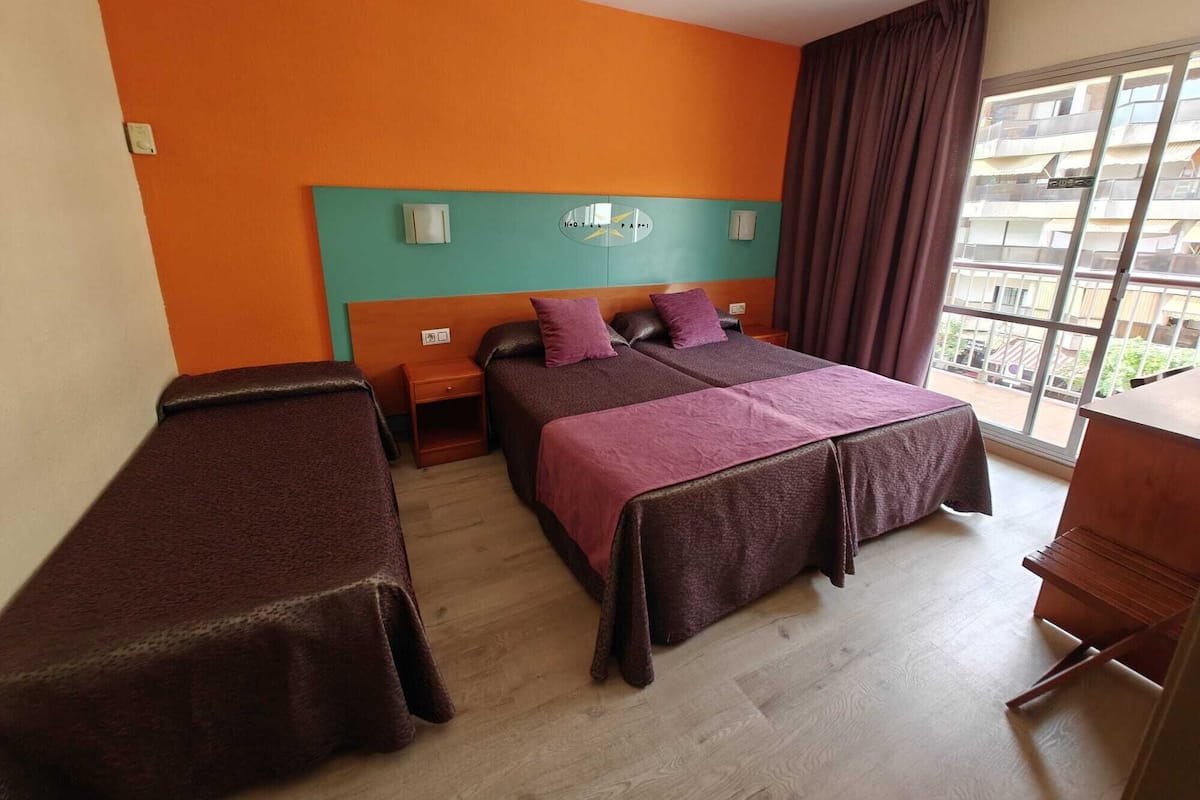 Ett hotellrum med två sängar, ett stort fönster med utsikt, ett skrivbord i trä och en sänggavel med en spegel.