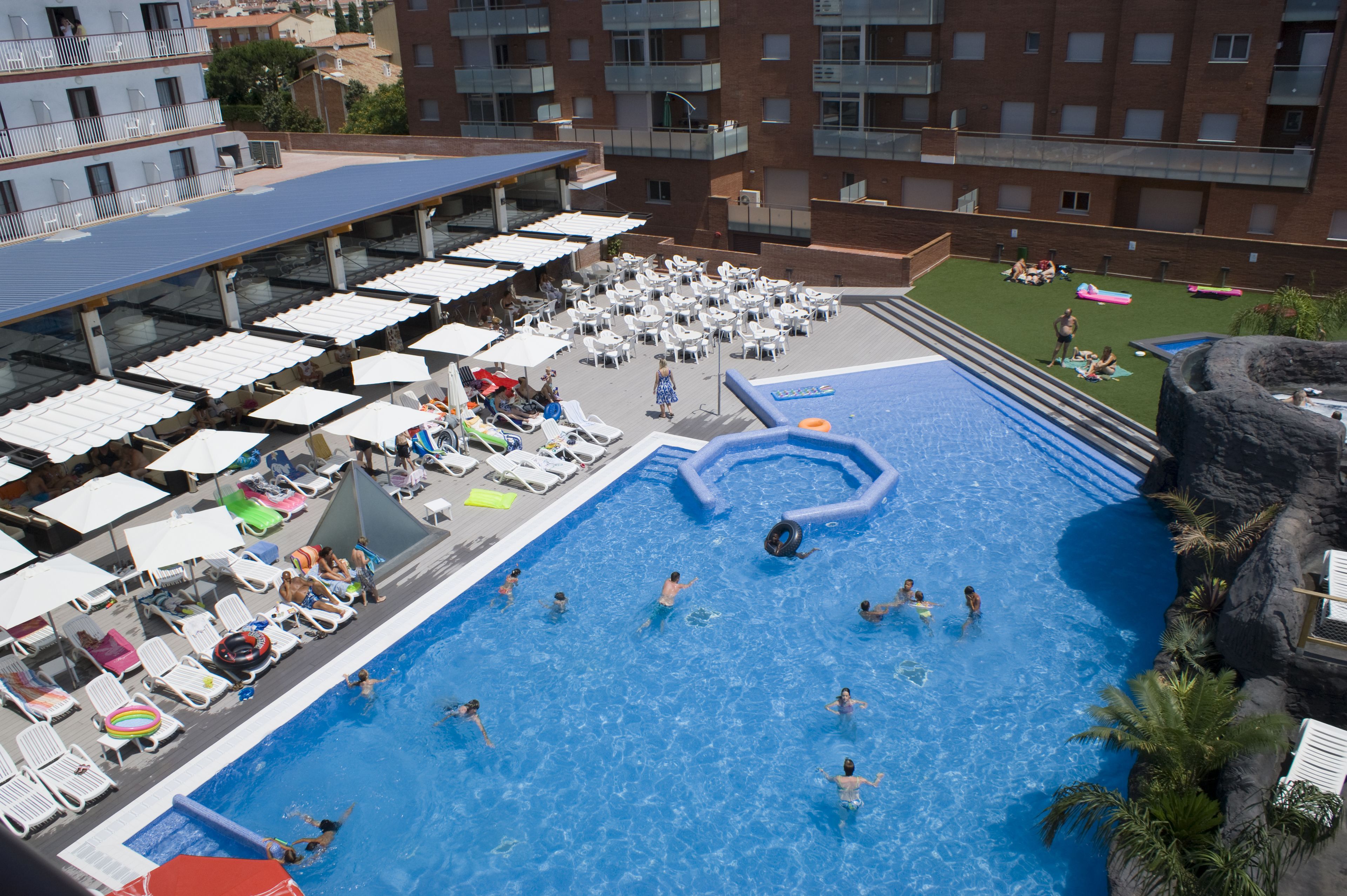 Un área de piscina en la azotea con varias piscinas, sillas de descanso y sombrillas.