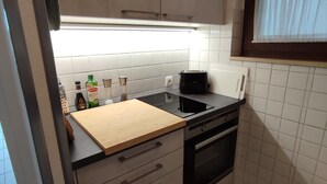 Kompakti keittiö, jossa on puinen työtaso, sisäänrakennettu uuni ja ikkuna, jossa on läpikuultavat verhot.
