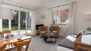 A cozy living room with a wooden dining table, wicker chairs, a sofa, and a television.