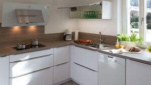 A modern kitchen with white cabinets, a stainless steel range hood, a coffee maker, and a window with a view of greenery.