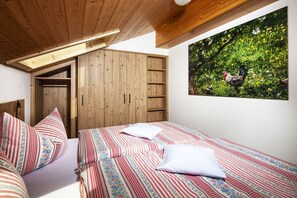 A bedroom with a wooden wardrobe, a bed with striped bedding, and a wall-mounted picture of chickens in a field. - Watzmann, 1-4 Pers., ca. 70 qm, 2 Schlafzimmer, 2x Dusche/WC, Bauernstube, Küche, Balkon (Bischofswiesen)