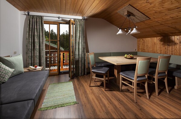 A cozy room with a wooden ceiling, a sofa, a dining table with chairs, and a view through a glass door. - Watzmann, 1-4 Pers., ca. 70 qm, 2 Schlafzimmer, 2x Dusche/WC, Bauernstube, Küche, Balkon (Bischofswiesen)