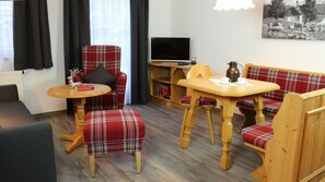 Une pièce meublée comprenant un canapé, deux fauteuils à motifs écossais, une petite table, un téléviseur et une bibliothèque.