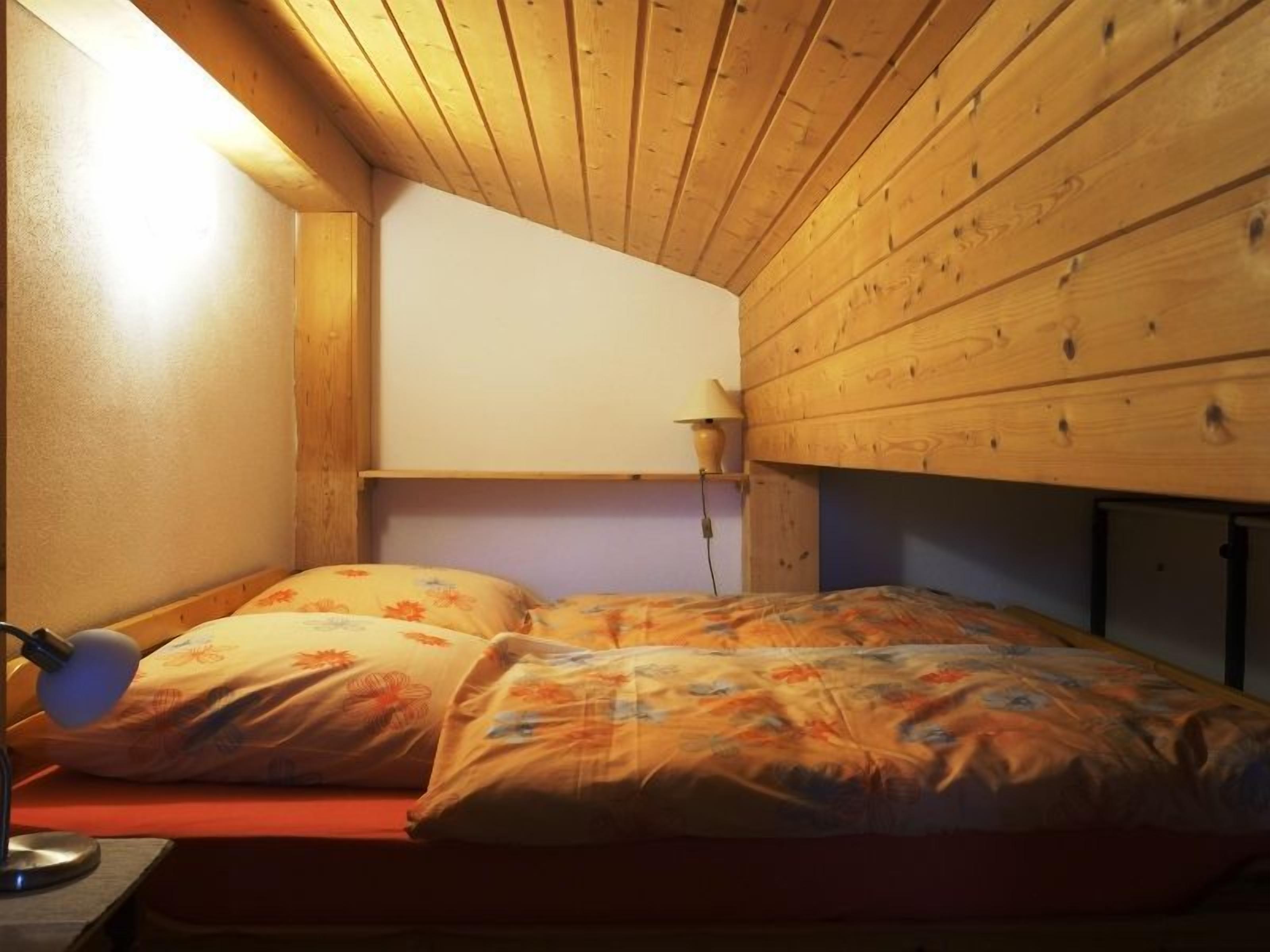 Una cama individual con una colcha estampada floral en una habitación con paredes de madera y techo inclinado.
