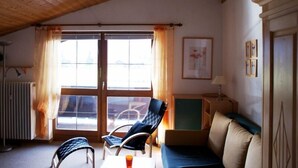Ett mysigt rum med ett sluttande tak, en soffa, ett bord med en stol och en vacker utsikt genom stora fönster.
