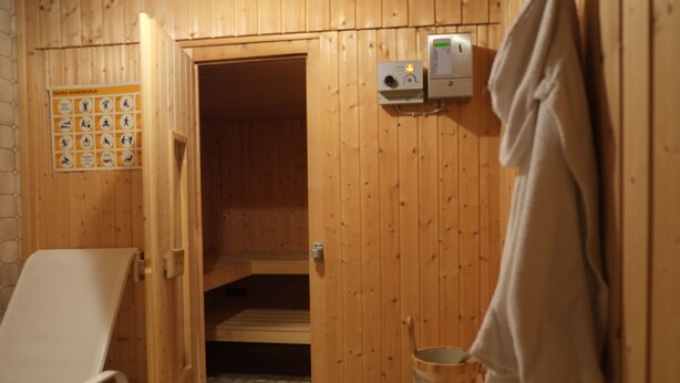 Ett ångrum med träväggar, en handduksställning, en kontrollpanel för ångrummet och en ångbänk.
