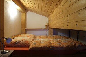 A small, cozy bedroom with a wooden ceiling, a single bed with floral bedding, and a bedside lamp.