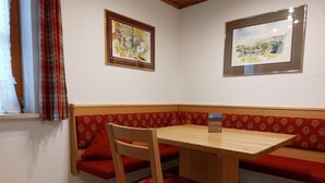 A corner seating area with a wooden table and a chair, red patterned cushions, and two framed paintings on the wall. - Ferienwohnung 3 (Berchtesgaden)
