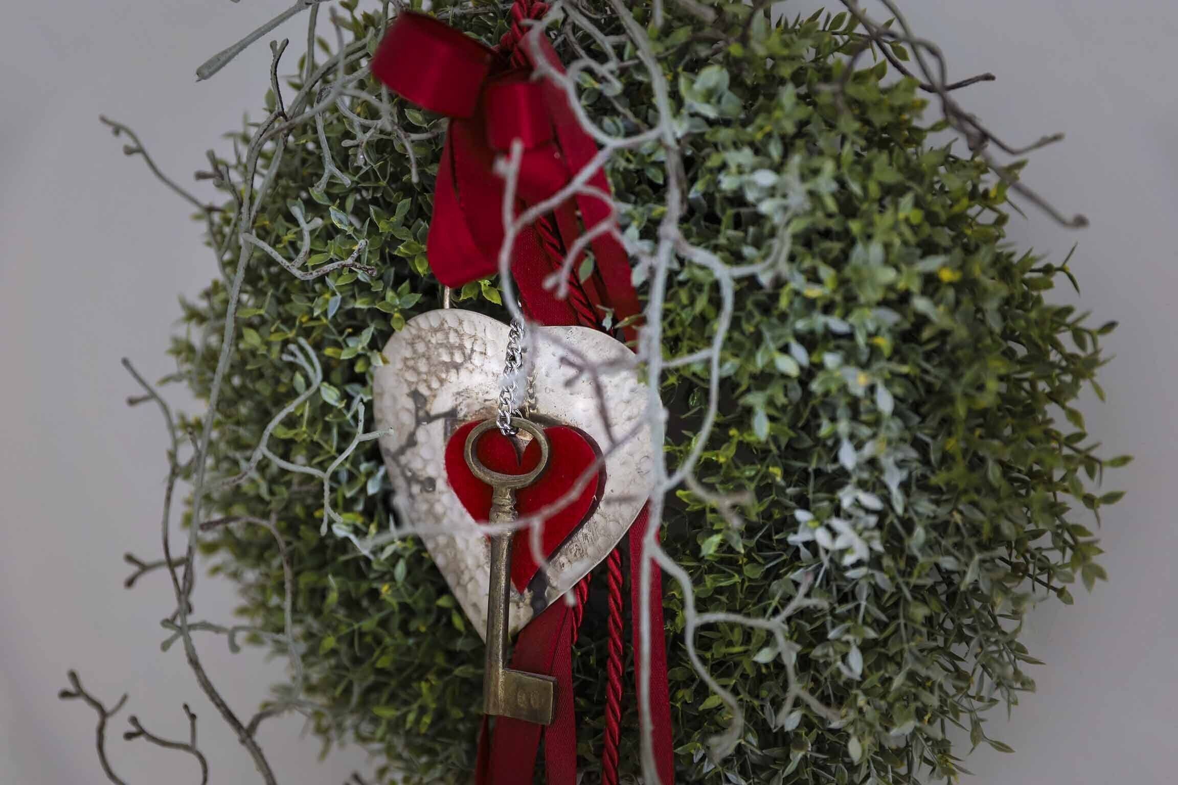 A heart-shaped keychain hanging from a red ribbon, surrounded by green foliage.