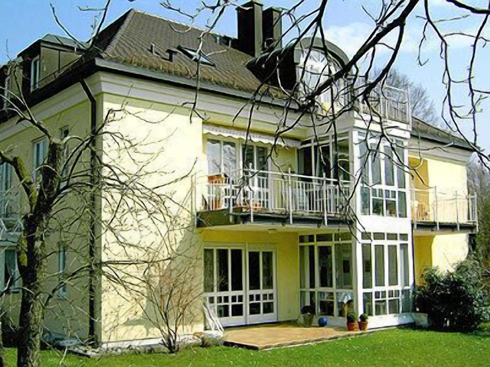 A two-story house with a balcony, large windows, and a well-maintained lawn.