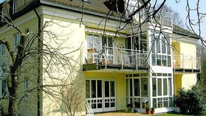 Une maison à deux étages dotée d’un balcon, de grandes fenêtres et d’une pelouse bien entretenue.