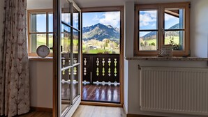 A room with a wooden floor, a clock, a window with a view of mountains, and a radiator. - Apartment no. 6, 1-4 persons, 60 sqm, balcony, W-LAN, 1 bedroom and 1 children's bedroom (Ramsau bei Berchtesgaden)
