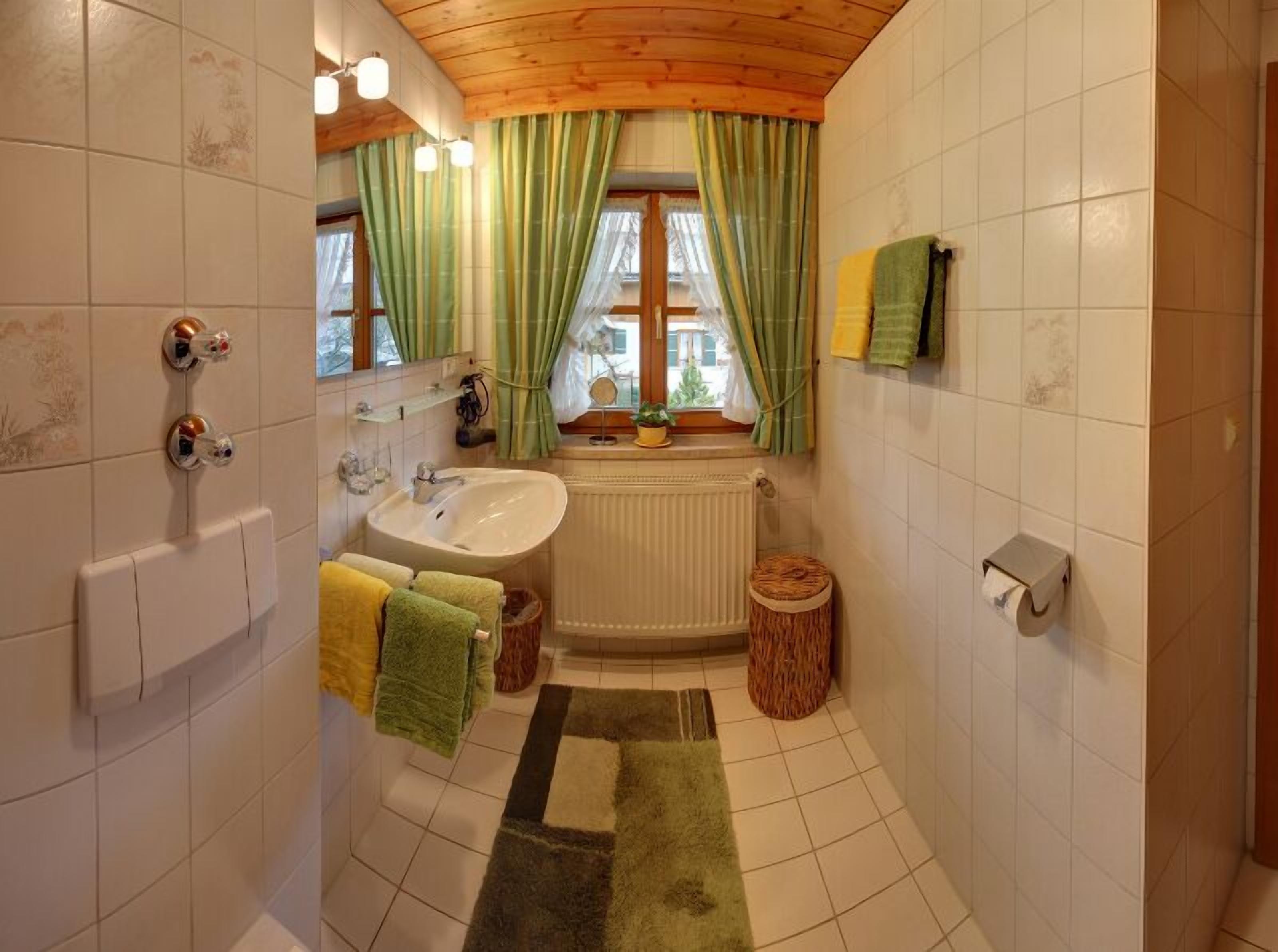 A bathroom with a sink, mirror, green curtains, a window, and a radiator.