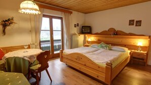 Une chambre confortable avec un lit en bois, une petite table avec une chaise, une télévision et une fenêtre avec des rideaux.