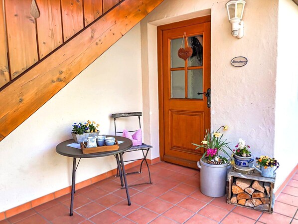A wooden staircase, a wooden door, a small table with cups and flowers, and potted plants.