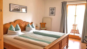 A bedroom with a wooden bed, striped bedding, a chair, a radiator, and two framed pictures on the wall. - Ferienwohnung I 45 qm°, zwei Schlafzimmer, Südbalkon und ebenerdigem Eingang° (Aschau im Chiemgau)