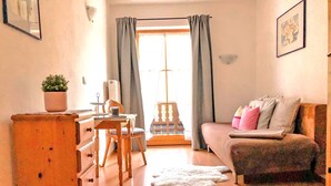 A cozy room with a wooden dresser, a desk with a chair, a sofa with pillows, and a large window with curtains. - Ferienwohnung I 45 qm°, zwei Schlafzimmer, Südbalkon und ebenerdigem Eingang° (Aschau im Chiemgau)