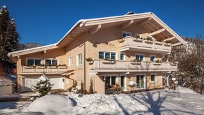En tvåvånings chalet med en balkong på övre våningen, ett garage och ett snötäckt landskap.