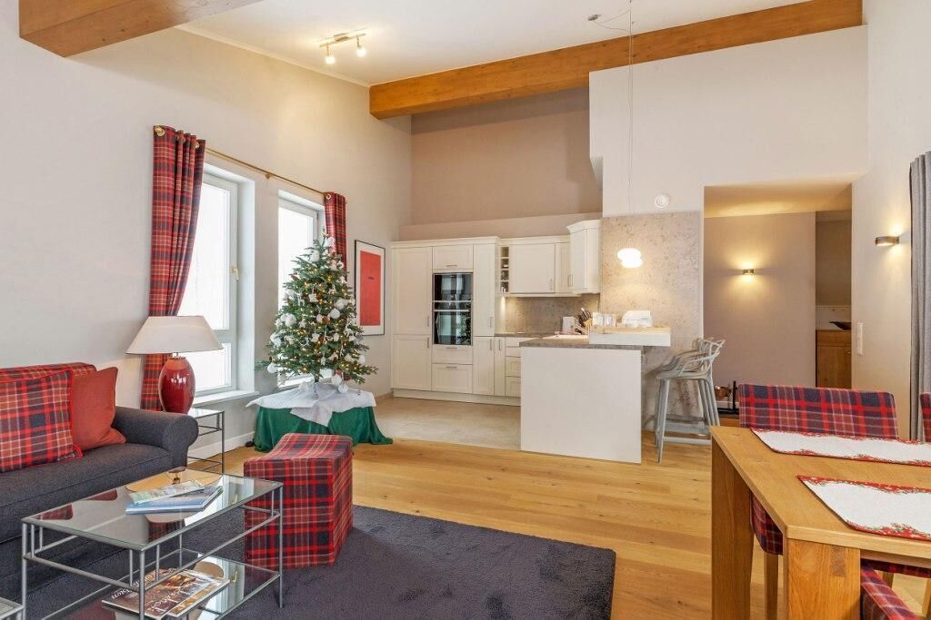 Een moderne woonkamer met een bank, salontafel en een kleine kerstboom. Er is een keuken met witte kasten en een eettafel met geruite tafelkleden.