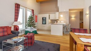 Ett modernt vardagsrum med en soffa, ett soffbord och ett litet julgran. Här finns också en köksdel med vita skåp och ett matbord med rutiga dukar.