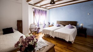 Een kamer met twee bedden, een houten vloer, een stoel, een tafel met bloemen en een raam met gordijnen.