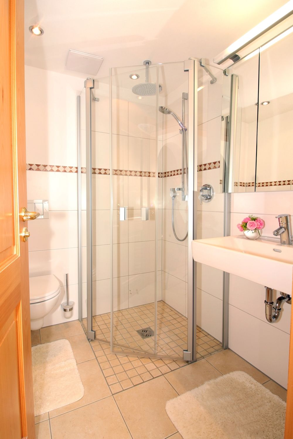Uma casa de banho moderna com chuveiro em cabine de vidro, lavatório branco com espelho e sanita.