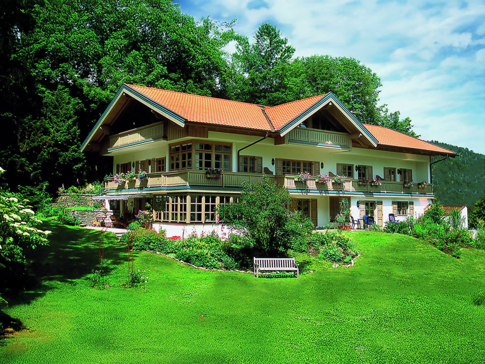 A large, two-story house with a red-tiled roof, surrounded by lush greenery and trees.