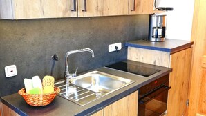 Une cuisine avec des meubles en bois, un évier en acier inoxydable, une machine à café et un panier contenant des produits de nettoyage.