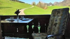 Un coin repas avec une table dressée pour deux personnes, une chaise et une vue sur un paysage verdoyant avec une route.