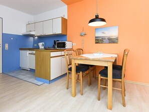 A compact kitchen with white cabinets, a microwave, and a coffee maker. There is a dining table with four chairs and a hanging light fixture above.