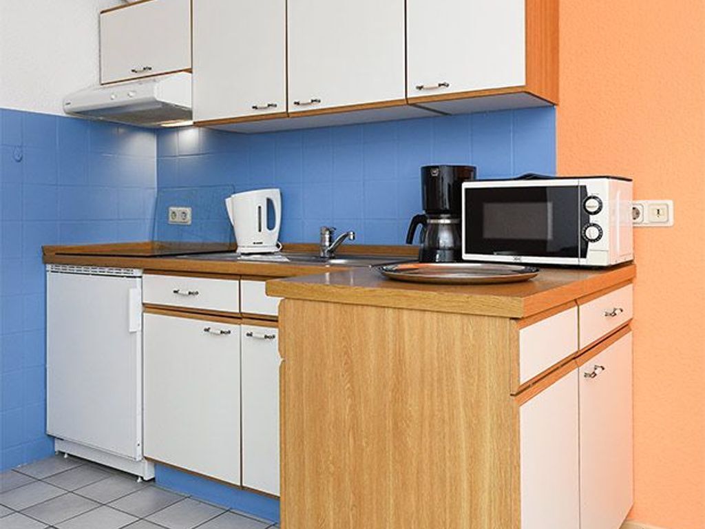 A compact kitchen with white cabinets, a wooden countertop, a coffee maker, and a microwave.