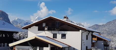A two-story chalet with a sloped roof, a balcony, and a ski lift in the foreground.