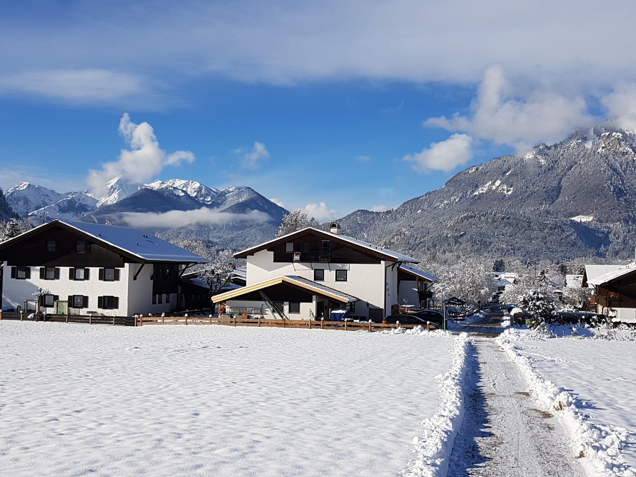 Un villaggio innevato con edifici in stile chalet tradizionale, cielo sereno e montagne innevate sullo sfondo.
