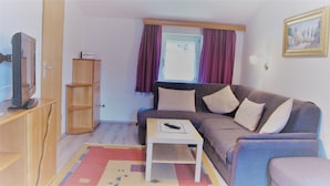 A living room with a sofa, a coffee table, a TV, and a bookshelf. - Ferienwohnung Grünstein, 1 bis 2 Personen, 54 qm, 1 Schlafzimmer, extra Küche, Balkon (Schönau am Königssee)