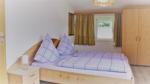 A bedroom with a wooden bed, a nightstand, a wardrobe, and a window with curtains. - Ferienwohnung Grünstein, 1 bis 2 Personen, 54 qm, 1 Schlafzimmer, extra Küche, Balkon (Schönau am Königssee)