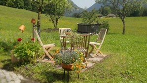 A garden with a wooden table and chairs, surrounded by flowers and plants. - Nr. 1, Ferienwohnung 2-4 Pers. mit 2 Schlafzimmern, Wohnküche, Dusche/WC und Balkon (Bischofswiesen)