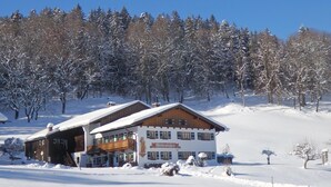 A snow-covered lodge with a wooden exterior and a balcony, surrounded by snow-laden trees. - Nr. 1, Ferienwohnung 2-4 Pers. mit 2 Schlafzimmern, Wohnküche, Dusche/WC und Balkon (Bischofswiesen)