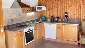 A compact kitchen with wooden cabinets, a microwave, a coffee maker, and a dishwasher. - Nr. 1, Ferienwohnung 2-4 Pers. mit 2 Schlafzimmern, Wohnküche, Dusche/WC und Balkon (Bischofswiesen)