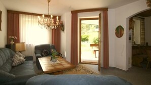 Un salon avec un canapé, une table basse et un lustre. Une porte donne accès à un espace extérieur où se trouve un banc.