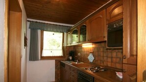 Une cuisine de taille réduite, dotée de meubles en bois, d’un four encastré et d’une fenêtre avec des rideaux.