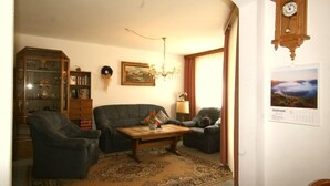Un salon comprenant un canapé, des fauteuils, une table basse, un lustre, une horloge et un tableau encadré accroché au mur.