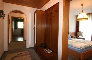 Une chambre avec une armoire en bois, un lit recouvert d’une couvre-lit à rayures, une table de chevet et une lampe suspendue.