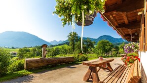 A rustic outdoor seating area with a wooden table and bench, surrounded by greenery and a mountainous backdrop. - Apartment Alm Stüberl, 65 square meters, balcony, 2 sep. Bedroom, max. 4 pers. (Ruhpolding)